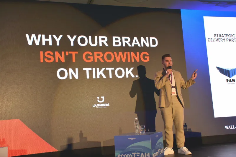 Cristi Jumară pe scenă, cu microfonul în mână, în fața slide-ului „Why your brand isn’t growing on TikTok”.