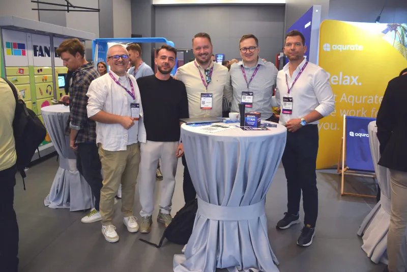 Grup de participanți la o masă înaltă în zona de expoziție, în mijlocul unei conversații.