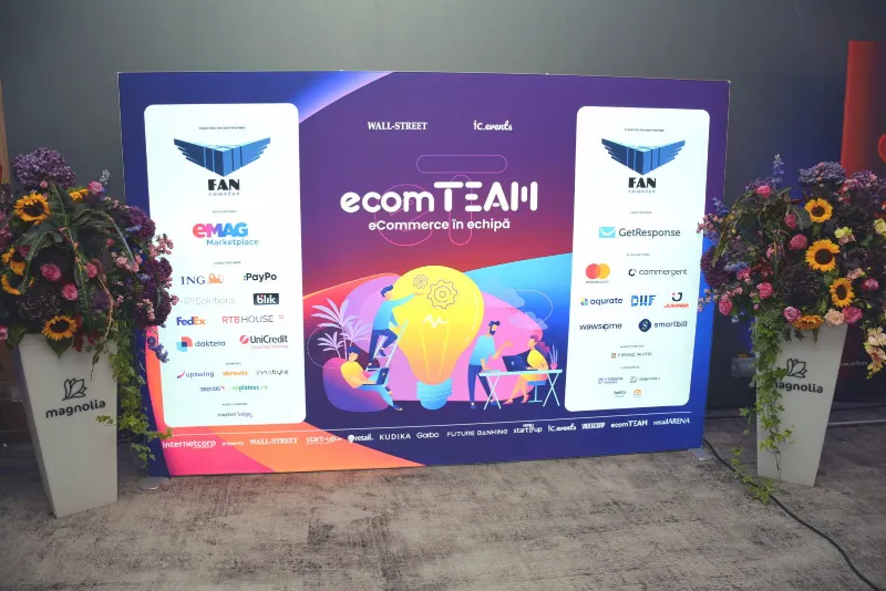 Panoul foto ecomTEAM „eCommerce în echipă”, cu siglele partenerilor, încadrat de aranjamente florale.